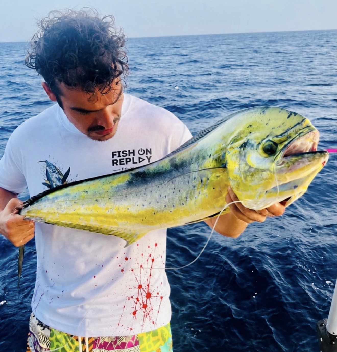 Pescador a bordo con una captura, con camiseta Fish On Replay